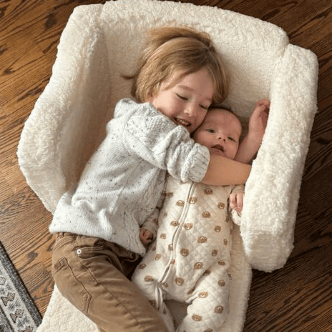 Image of a child hugging their younger baby sibling in a sherpa couch