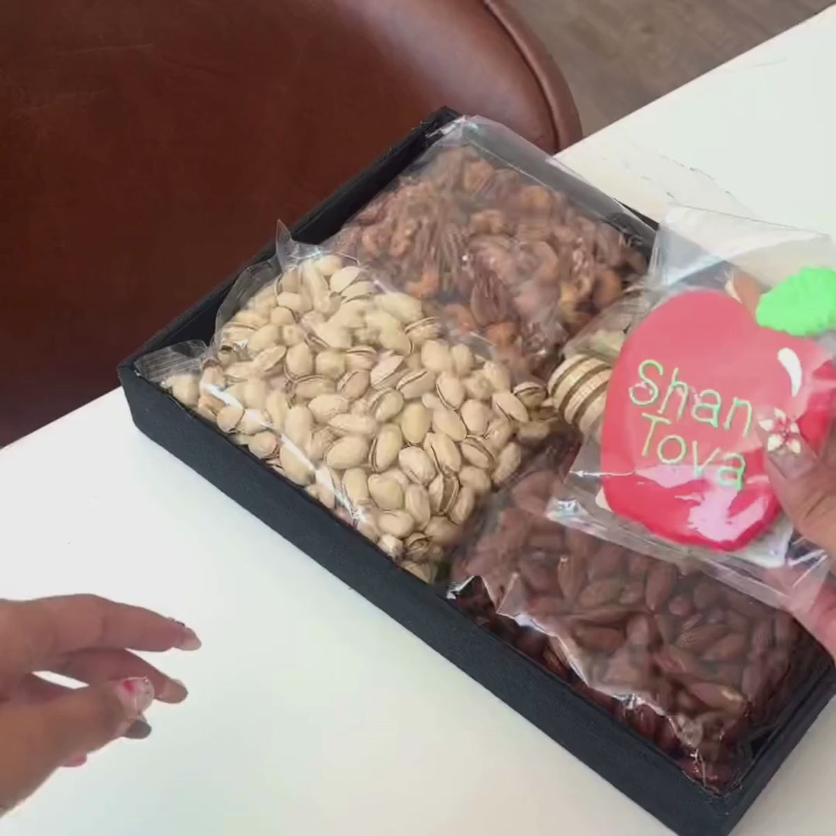 Hands unpacking a 6-piece Sweet Harvest Nut Tray, displaying Wendell Estate Raw Honey, a Hand-Painted Shana Tova Apple-Shaped Cookie, and an array of nuts for the perfect festive indulgence. 
