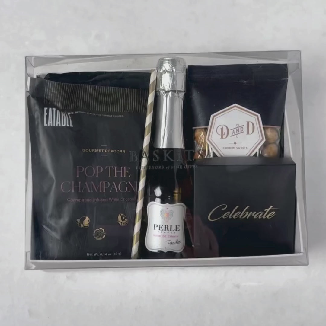 Hands unpacking a 6-piece Cheers Non Alcoholic gift box, displaying a mini bottle of Perle Non-Alcoholic Rosé, and an array of celebratory indulgences.