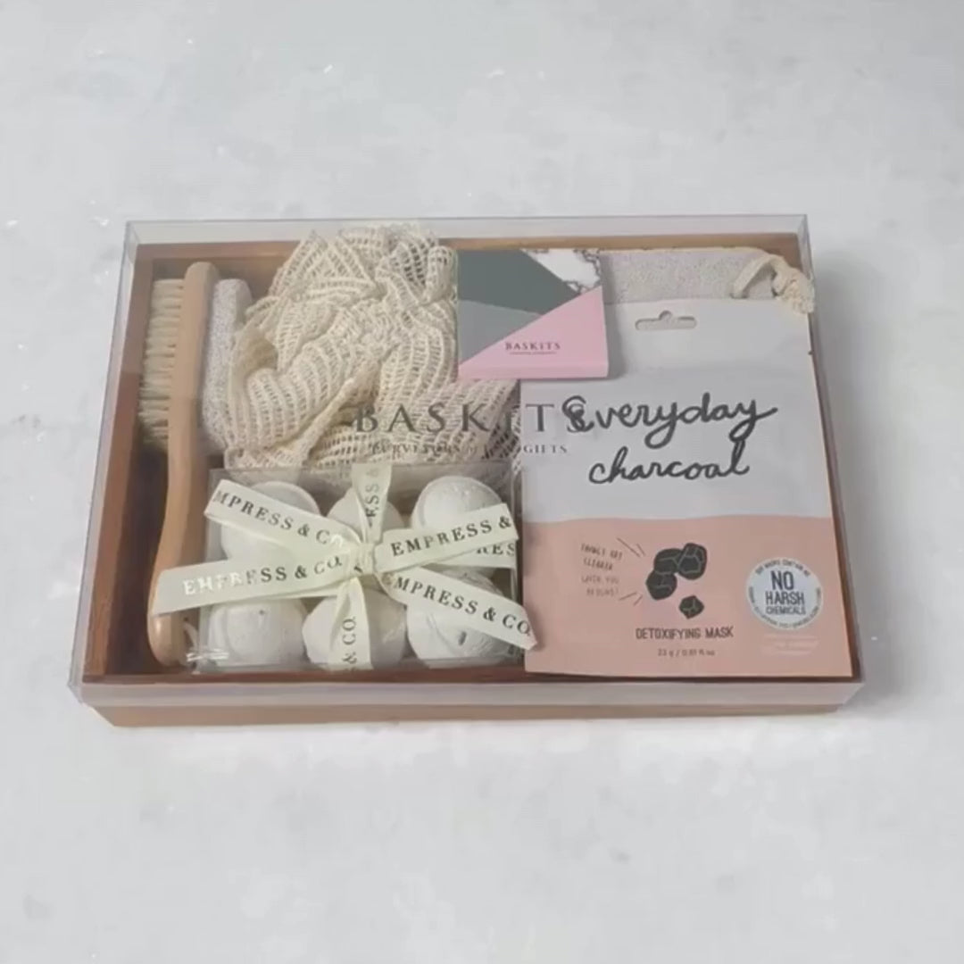 Hands unpacking a 7-piece Spa Essentials gift box, displaying our Lavender Bath Bombs and an array of relaxing spa indulgences.