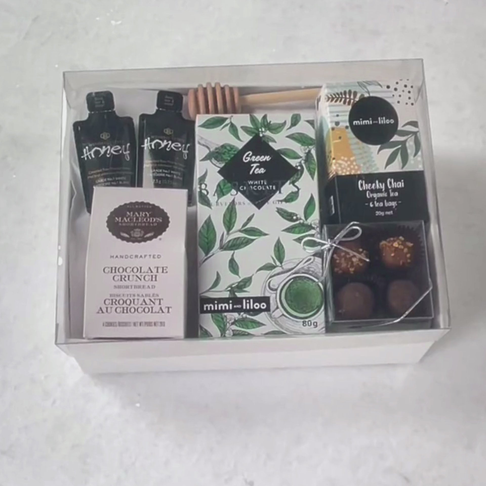 Hands unpacking a 7-piece Just Tea & Me gift box, displaying Mary Macleod's famous Chocolate Crunch Cookies, and an array of essential comforting indulgences. 