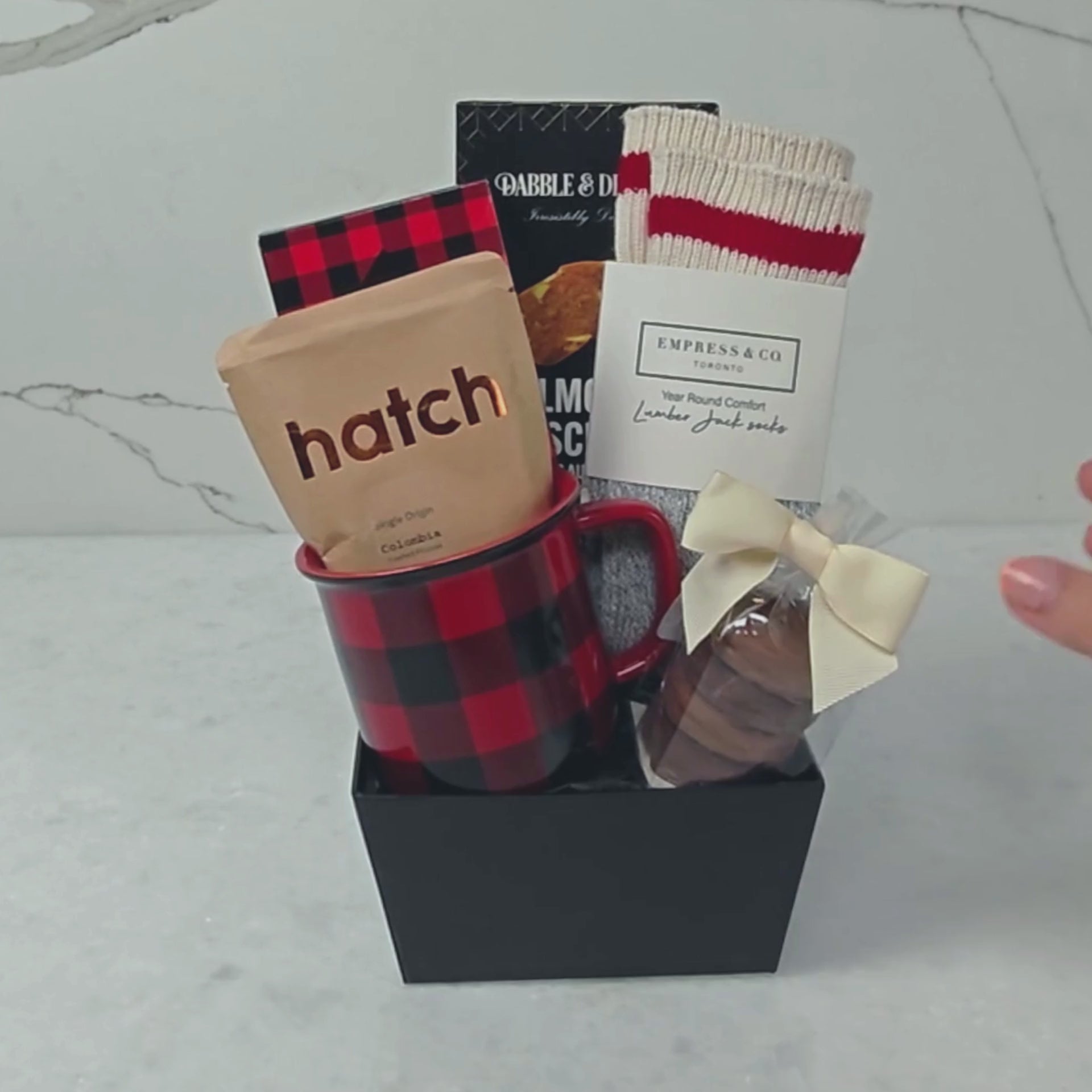Hands unpacking a 7-piece Just For You gift basket, displaying our signature Dabble & Drizzle Butter Almond Biscuits, and an array of curated indulgences.