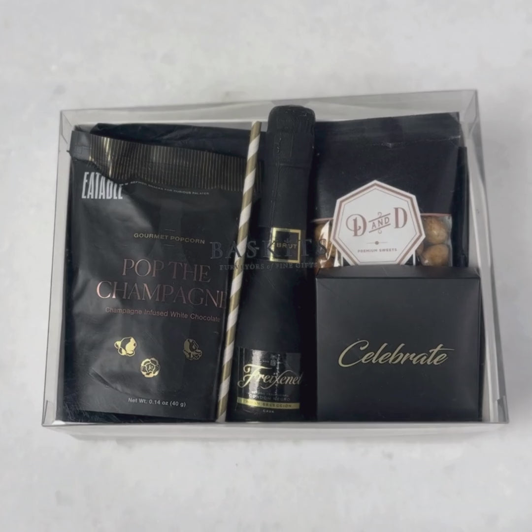 Hands unpacking a 6-piece Cheers gift box, displaying a mini bottle of Freixenet Cordon Negro Brut Cava, and an array of celebratory indulgences.