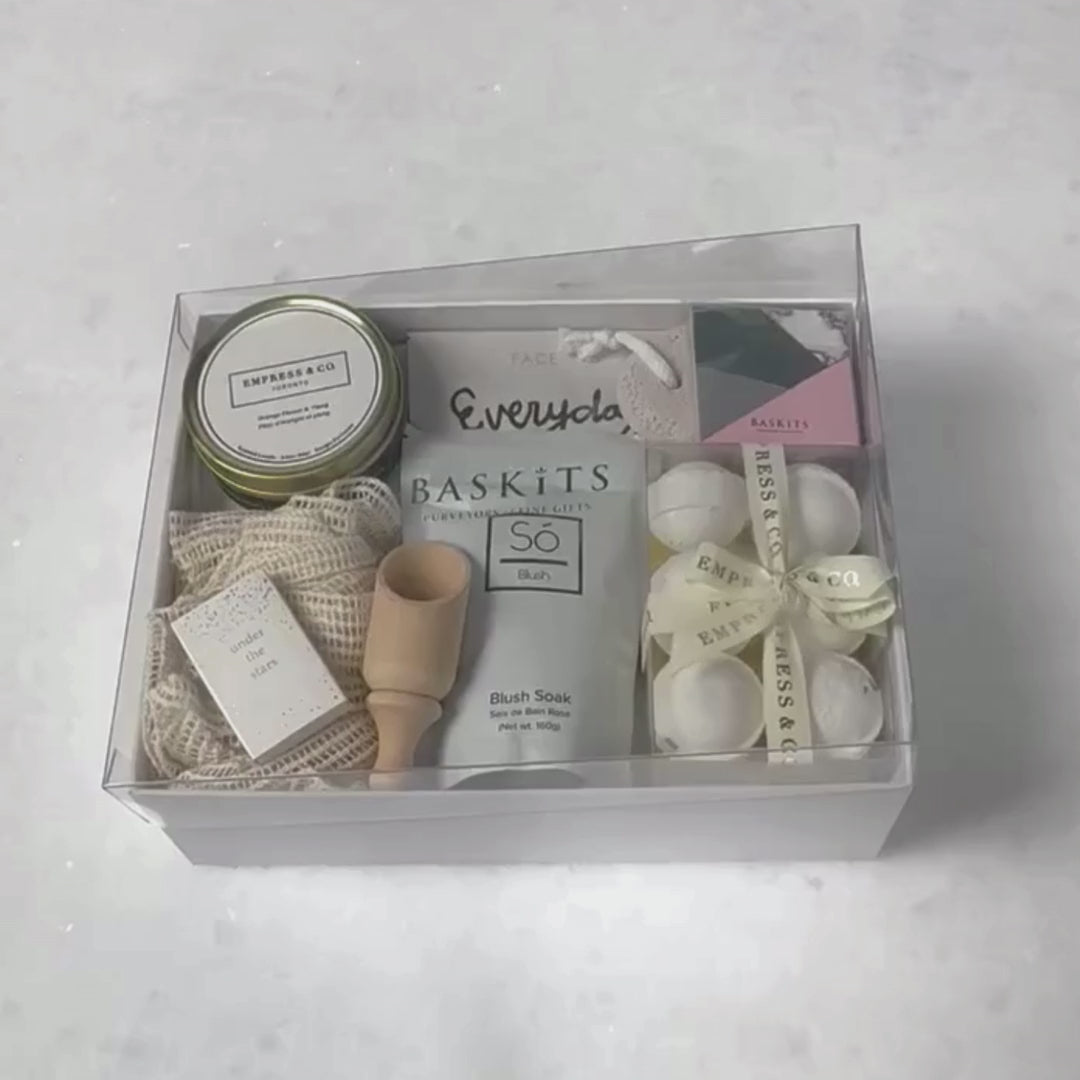 Hands unpacking a 10-piece Just Because gift box, displaying our Lavender Bath Bombs, and an array of essential spa items.