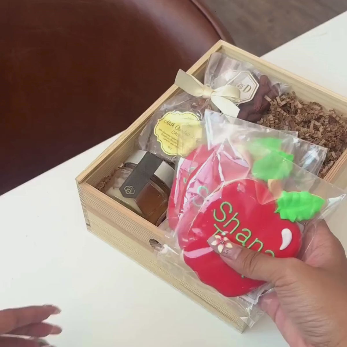 Hands unpacking a 6-piece Golden Honey gift basket, displaying Wendell Estate Raw Honey, Hand-Painted Shana Tova Apple-Shaped Cookies, and an array of festive indulgences. 